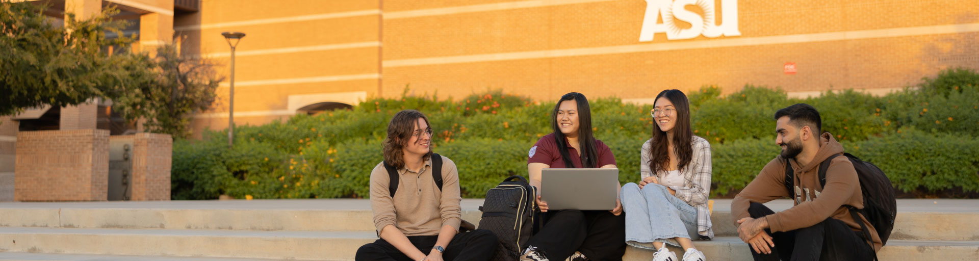 students gathered to view a laptop screen while sitting outside