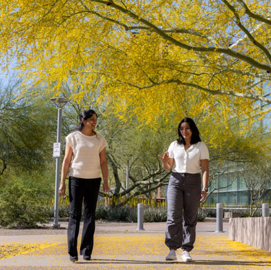 two people walking on a path near trees with yellow leaves